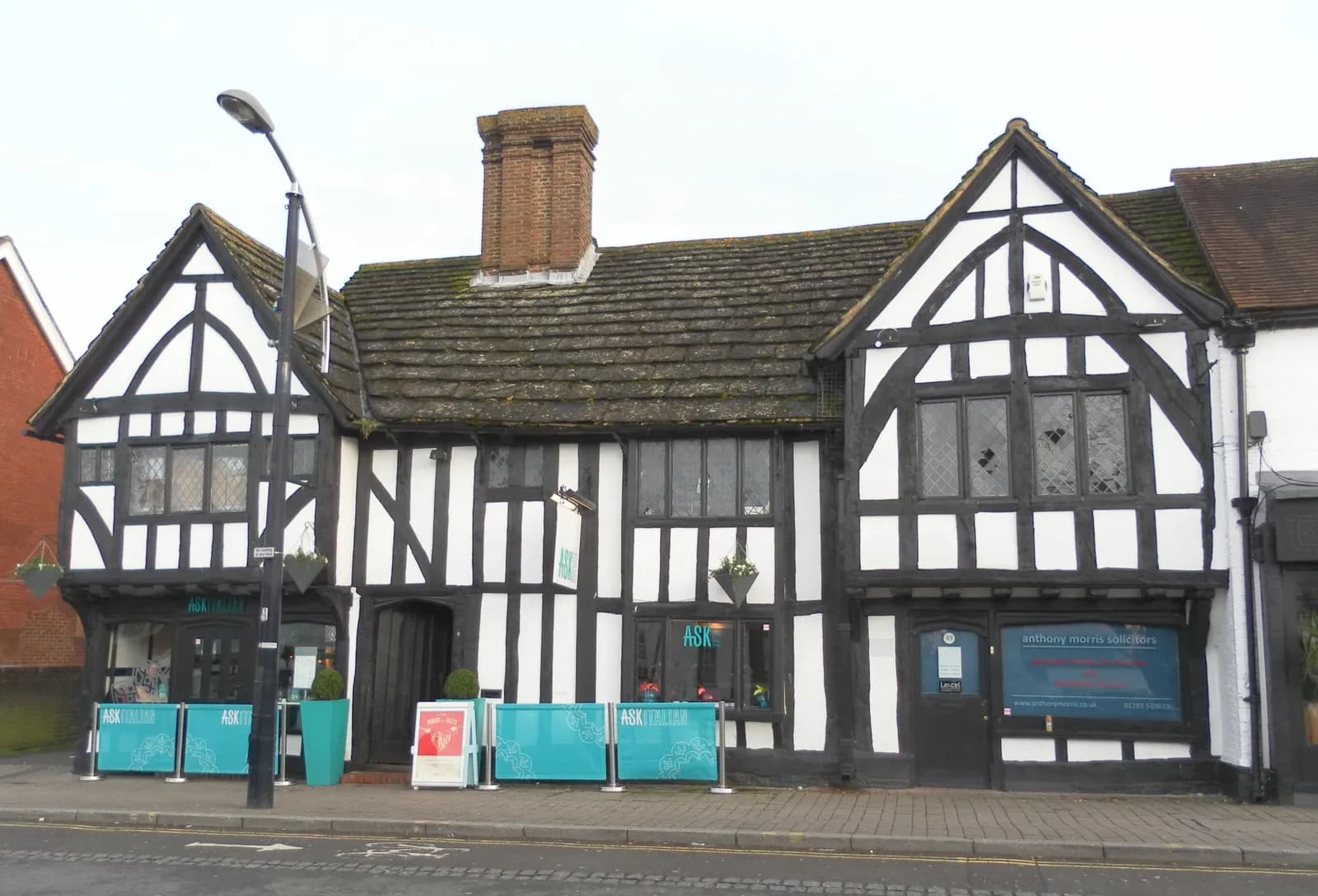 A historic, two-story timber-framed building with a gabled roof, white infill panels, and exposed black timber beams, functioning as a restaurant and office space.